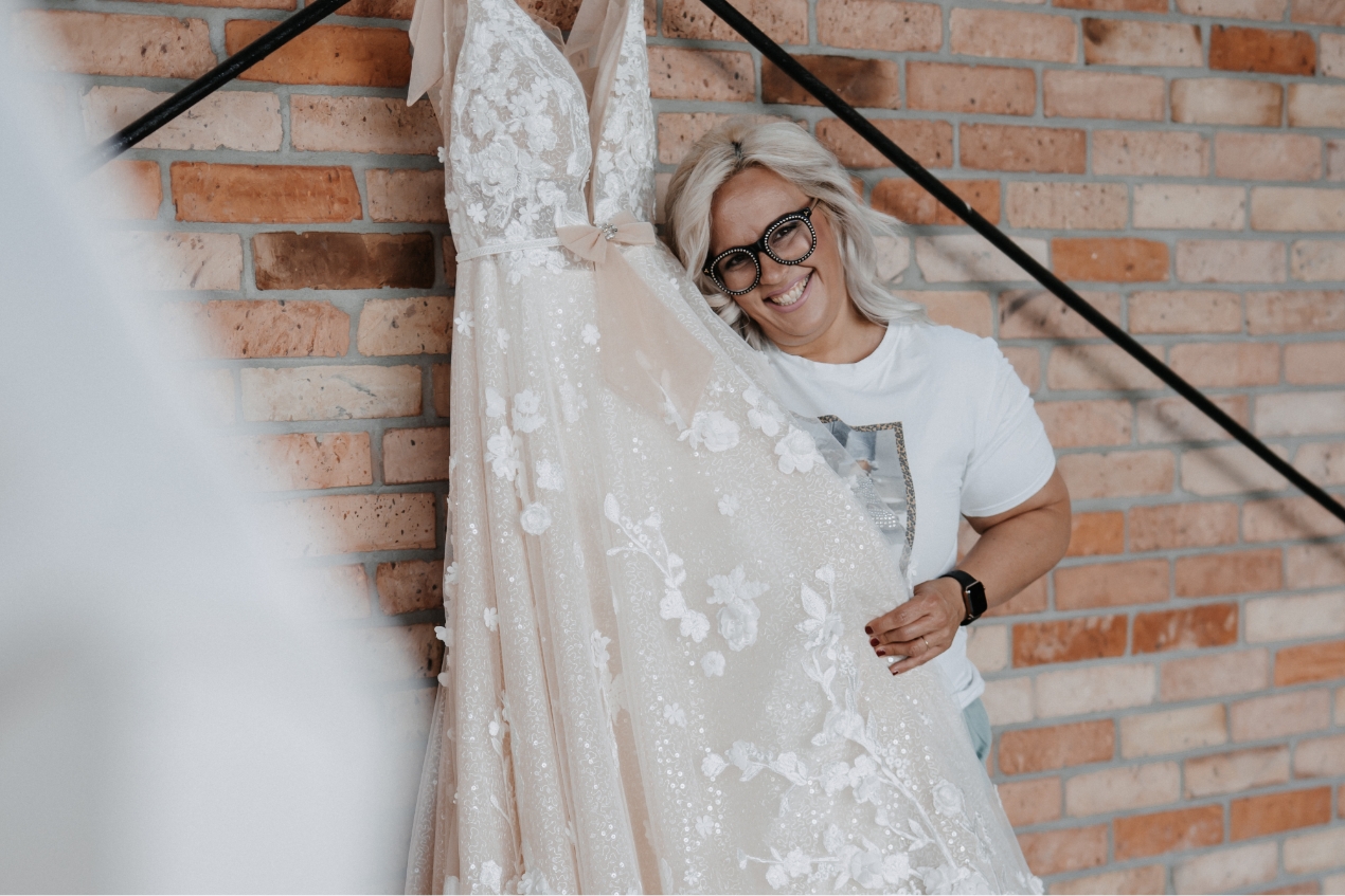 Frau präsentiert ein Brautkleid vor einer Backsteinwand